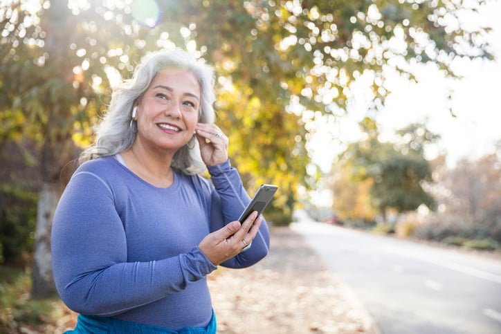 Older woman puts in her earbuds right before beginning her outdoor run