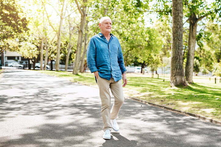 A senior man walks on a tree lined path in summer