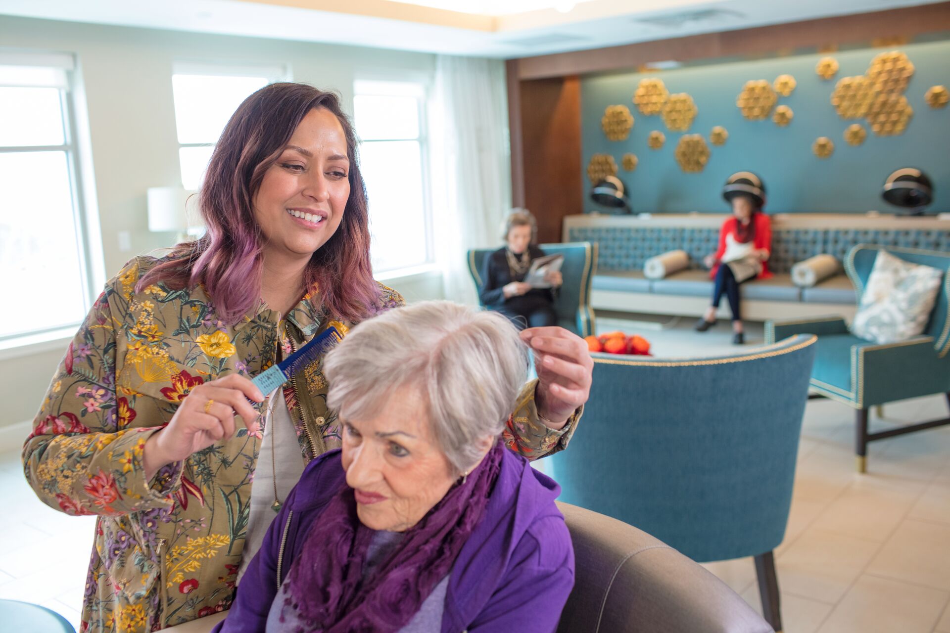 A hair stylist works on a senior woman's hair